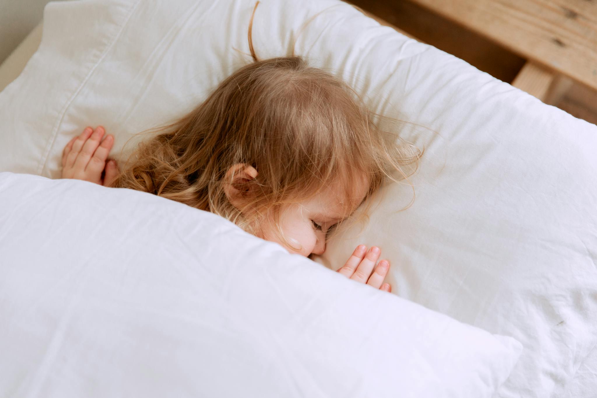 High angle of crop unrecognizable barefooted ethnic baby lying on soft bed at home in daylight
